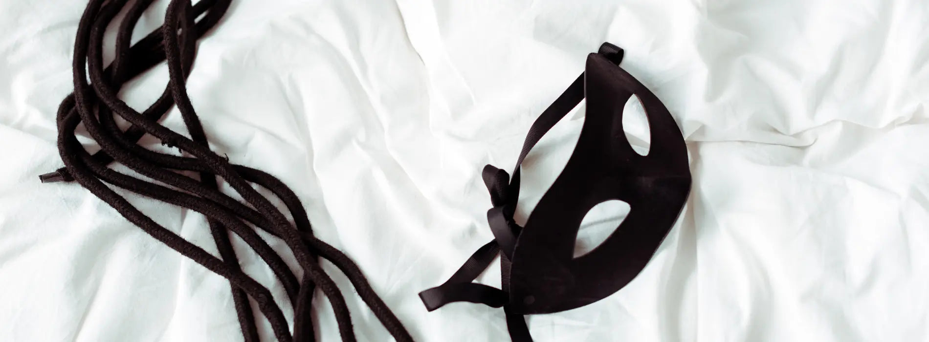 Accessoires BDSM posés sur un lit blanc : corde douce et masque noir élégants – image d’ambiance sensuelle et sobre, univers Solena