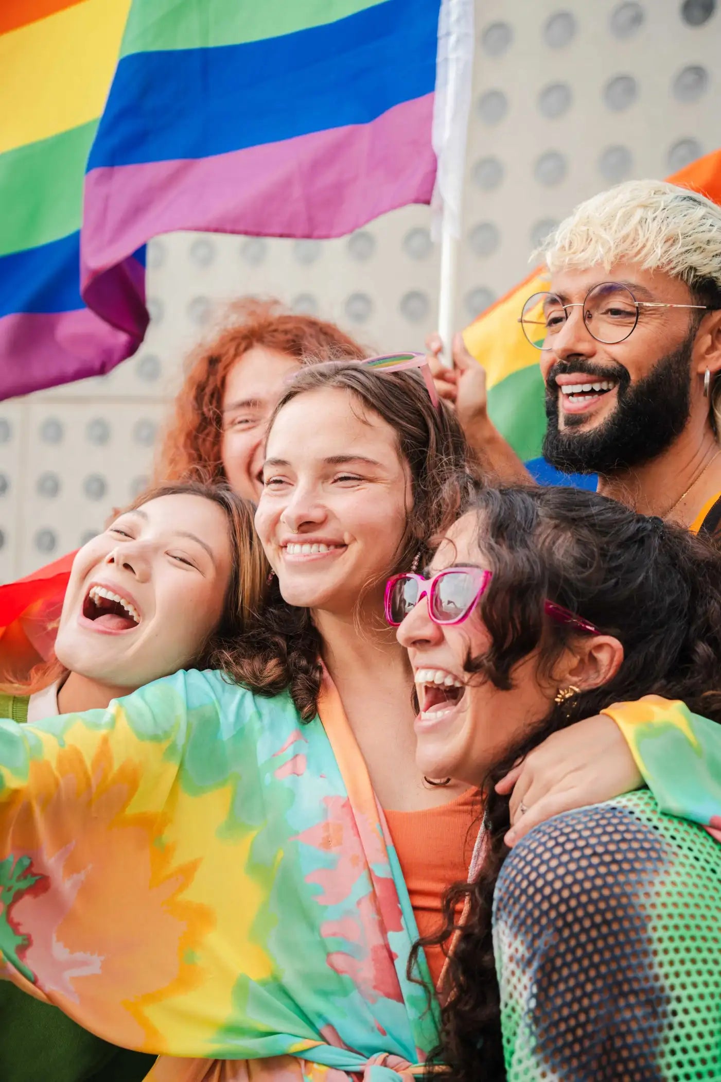 Groupe de personnes LGBTQ+ souriantes brandissant des drapeaux arc-en-ciel, symbolisant la diversité, la joie et l'inclusivité