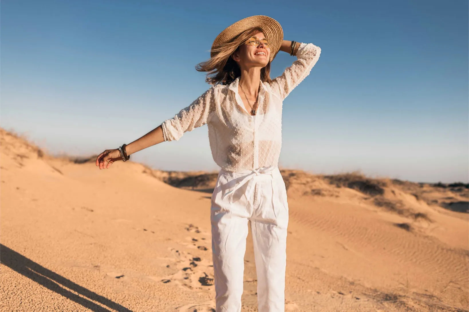 Femme souriante dans le désert, bras ouverts et visage tourné vers le soleil, incarnant la liberté et l’épanouissement intime offerts par Kyra, le vibromasseur double stimulation de Solena