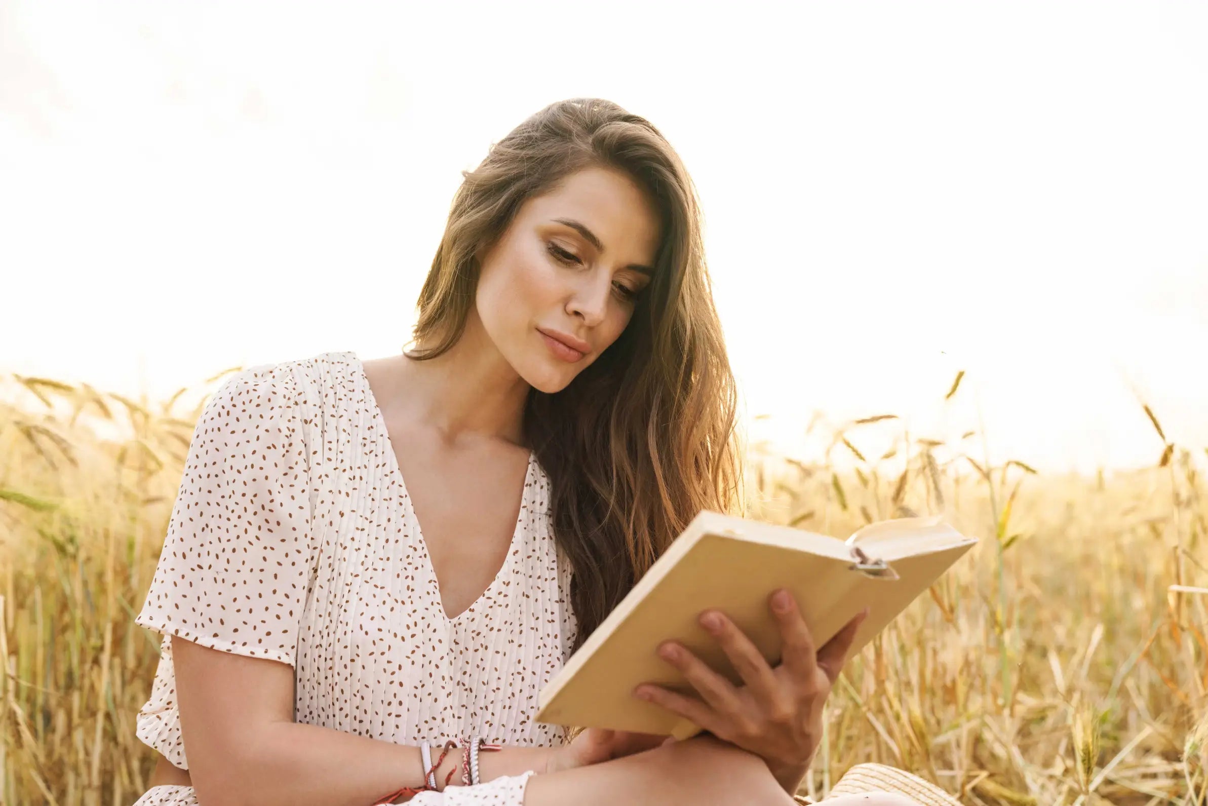 Femme assise dans un champ, concentrée sur un livre, illustrant la lecture d’un guide pratique pour découvrir et utiliser le vibromasseur 2-en-1 Lora de Solena en toute sérénité