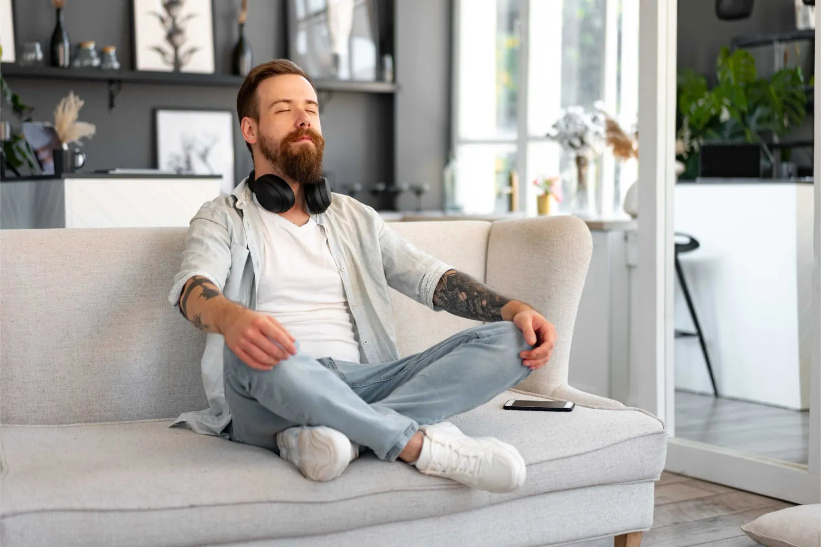 Homme détendu assis en tailleur sur un canapé, les yeux fermés, illustrant le bien-être intime et la relaxation procurés par le masturbateur Lumio de Solena