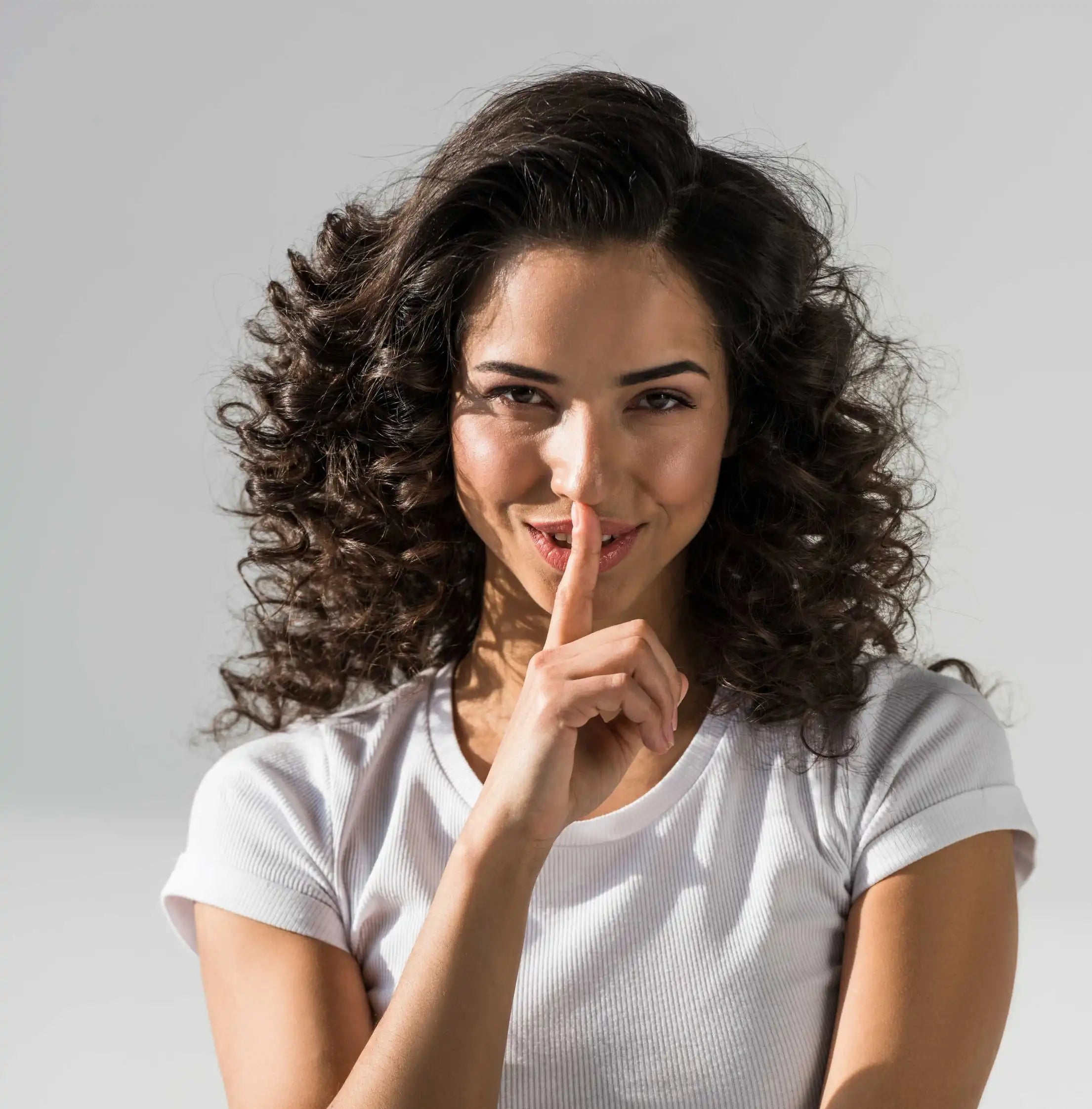 Femme souriante plaçant un doigt sur ses lèvres en signe de secret, évoquant la discrétion et le plaisir complice du vibromasseur télécommandé Luna de Solena