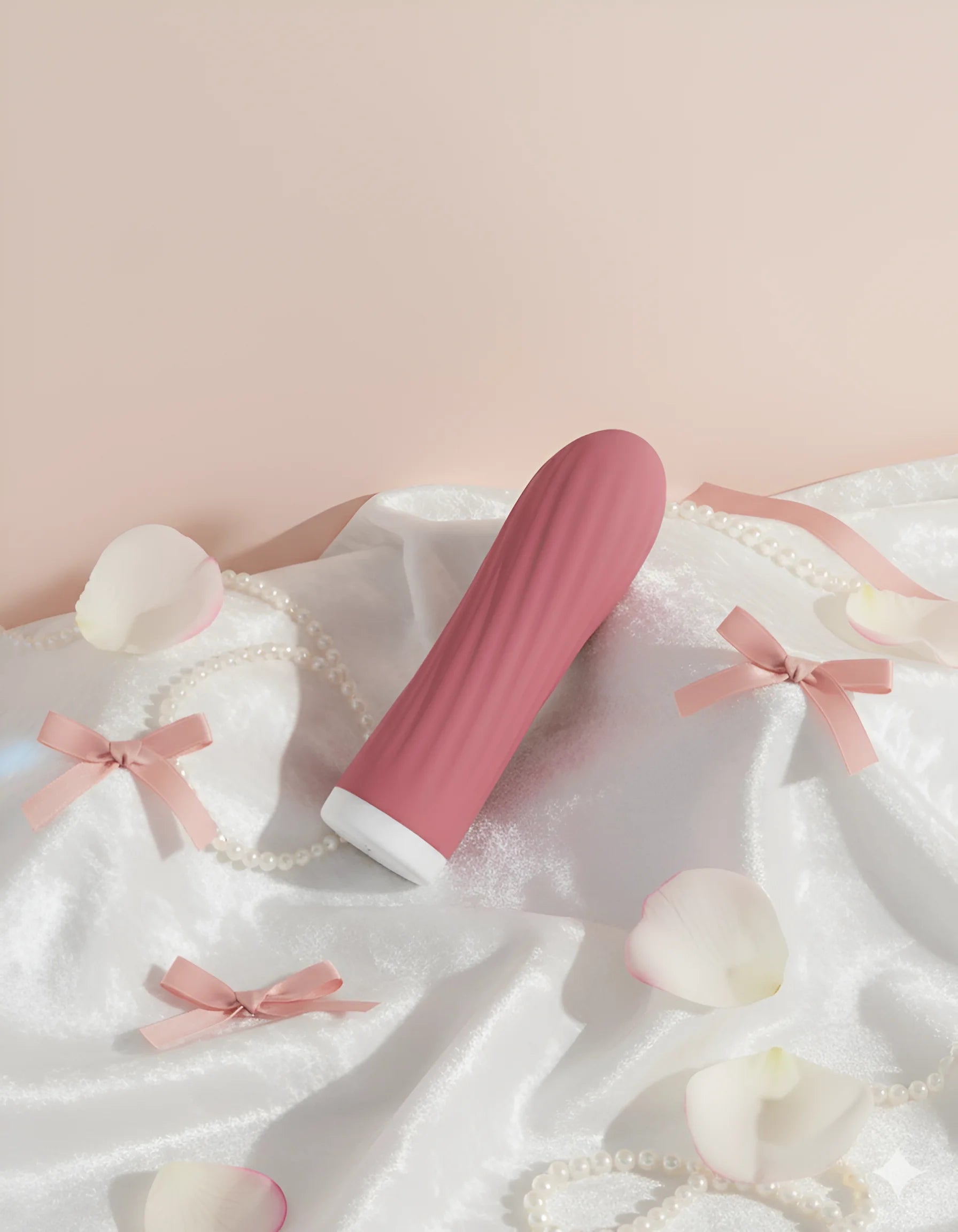 Vibromasseur de type Bullet (mini-masseur) Mira de Solena, de couleur rose et texturé, posé sur un tissu satiné blanc entouré de pétales et de rubans roses. Jouet sexuel discret et portable.
