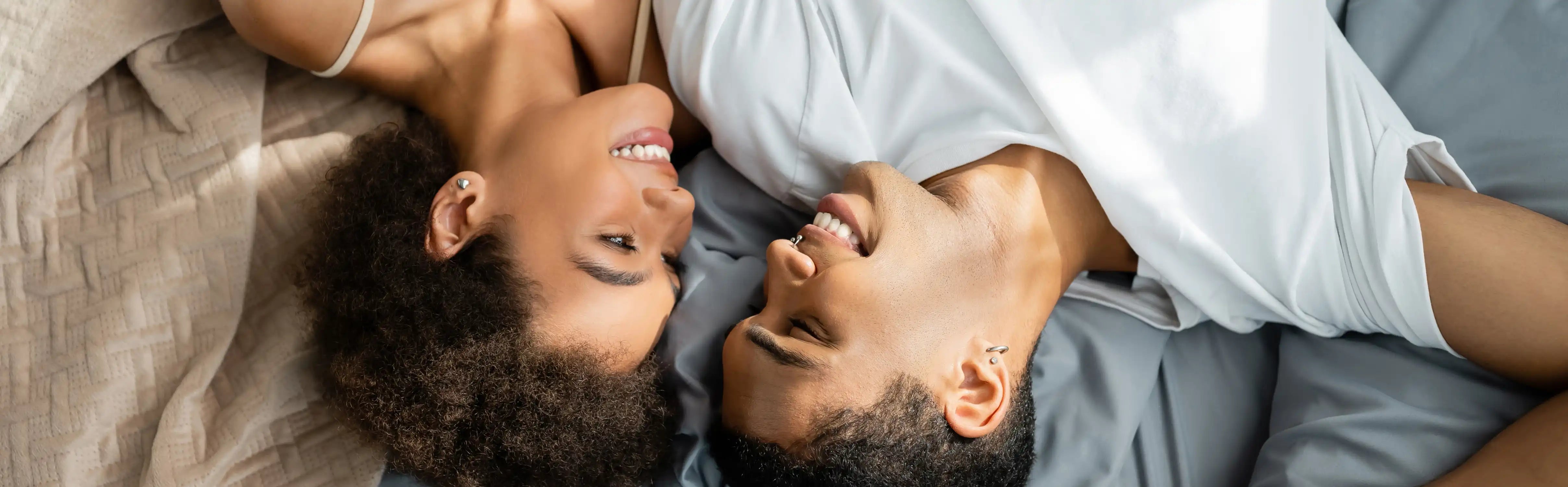 Couple allongé sur un lit, souriant et complice, illustrant l’intimité partagée et le plaisir à deux avec les sextoys pour couples Solena