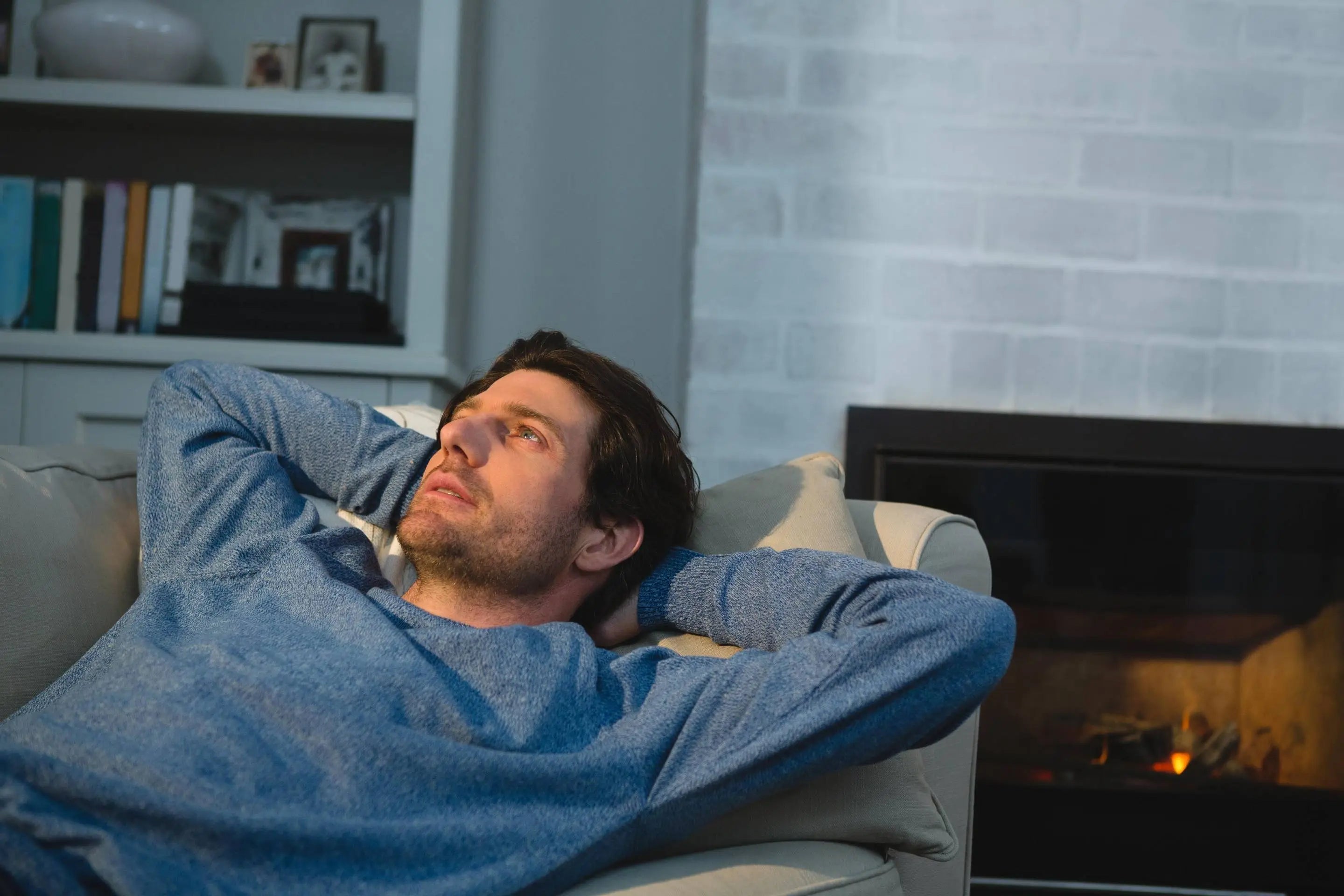 Homme détendu allongé sur un canapé près d'une cheminée, représentant le bien-être masculin et l'intimité avec Solena